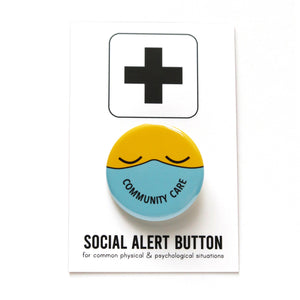Round button with a yellow emoji face with closed eyes, wearing a lavender mask that reads COMMUNITY CARE in the shape of a smile. Button is on a Social Alert Button backing card.