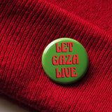 A round olive green pinback button that reads LET GAZA LIVE in a red art nouveau font. The button is pinned onto a red knit hat.