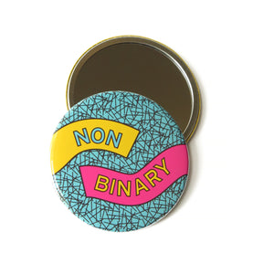 3" Round Pocket Mirror.  The other side of the mirror has a light blue patterned background with the words NON-BINARY in yellow and pink.