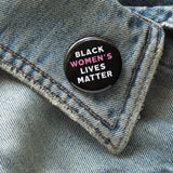 Round black pinback button that reads BLACK WOMEN'S LIVES MATTER, in white with Women's in pink for emphasis. Button is on a denim lapel.