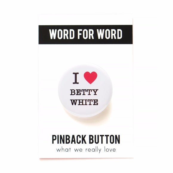 A shiny, round white pinback button with black serif text and a read heart, the button reads: I LOVE BETTY WHITE, with love being illustrated by a red heart. The button is on a black & white backing card that reads the brand name WORD FOR WORD at the top, and Pinback Button on the bottom