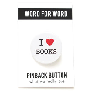 A round white pinback button that reads I LOVE BOOKS, love being represented by a red heart. Button is pinned to a Word For Word, What We Really Love branded backing card.