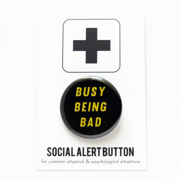 Round black pinback button that reads BUSY BEING BAD in yellow text . Badge is on a Social Alert Button backing card.
