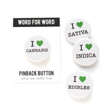 Four round white I heart pinback buttons with green hearts to indicate love. I Love Cannabis, I Love Sativa, I Love Indica, I Love Edibles. One button is on a Word For Word branded backing card.