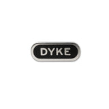 Capsule shaped enamel pin that reads DYKE in silver metal text with an silver outline on a black enamel background.