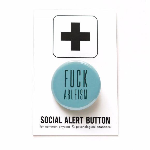 A pale turquoise shiny finback button that reads Fuck Ableism in a dark teal color, in a condensed sans serif font.  The pinback button is on a white backing card with a thick plus sign at the top of the card. On the bottom it reads Social Alert Button, for common physical & psychological situations.