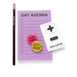 Lavender GAY AGENDA notepad with other queer gifts.  A purple GAY AGENDA pencil.  A black & silver QUEER enamel lapel pin.  And two pinback buttons that read: QUEER FEMME and GAY WAD.