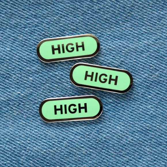 Three mint green capsule shaped enamel pins that read HIGH on a blue denim background.