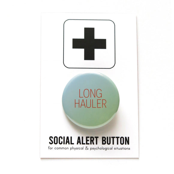 A round pale blue green pinback button that reads LONG HAULER in dark orange thin text. Button is on a SOCIAL ALERT BUTTON branded backing card. For Long Covid Awareness. 