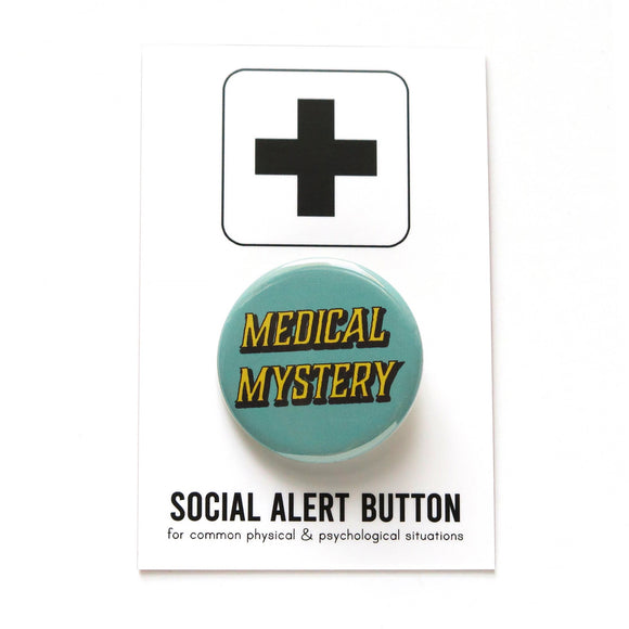 Round pinback button that says MEDICAL MYSTERY. Yellow shadowed text on a scrubs blue background.