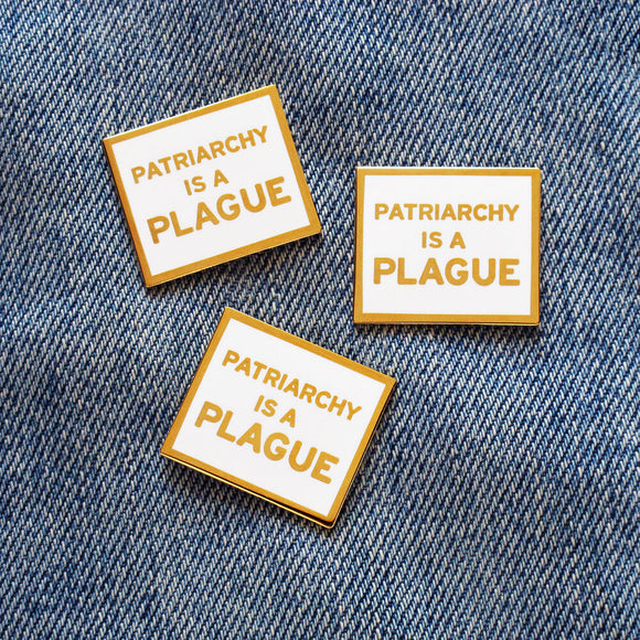 Three rectangle enamel pins that read PATRIARCHY IS A PLAGUE in gold metal & white enamel. Pins are on a blue denim jacket..