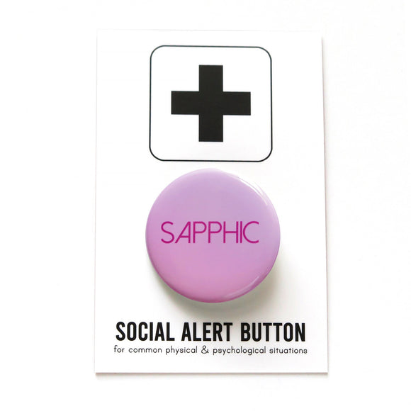 Round light lavender to pink pinback button with that reads SAPPHIC in a dark pink san serif font.  On a white backing card, black plus sign at the top. Below reads: Social Alert Button, with tiny text beneath it which says, for common physical & psychological situations