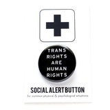 A round black pinback button that reads TRANS RIGHTS ARE HUMAN RIGHTS. Badge is pinned to a Social Alert Button branded backing card.