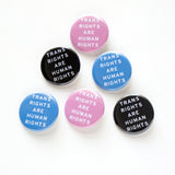 A mix of light blue, pink & black TRANS RIGHTS ARE HUMAN RIGHTS pinback buttons on a white background.