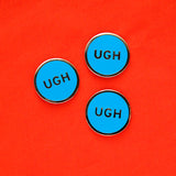 Three round, neon blue pins that say UGH, on a bright red fabric background.