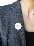 ALIVE pinback button pinned to the lapel of a gray blazer.