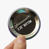 Back of a 2.25" metal pinback button, held up in a hand.