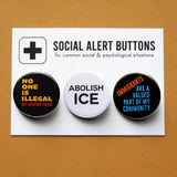 A Social Alert Buttons backing card with 3 immigration related pinback buttons attached, reading: No One Is Illegal on Stolen Land, Abolish Ice, Immigrants Are a Valued Part of My Community.