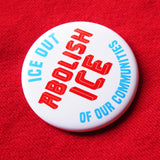 An angled round white 2.25" pinback button that reads ABOLISH ICE in thick red text in the center, and ICE OUT - OF OUR COMMUITIES in light blue text, above & below, curved to the round button.  Badge is pinned to a red sweatshirt.