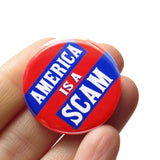 A round red pinback button with blue rectangles to pop white text that reads AMERICA IS A SCAM. Button is held in a hand.