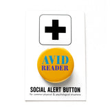 Round yellow colored pinback button which reads Avid Reader in pruple and teal text. The button is on a white Social Alert Button backing card with a black plus sign at the top.