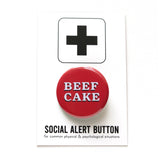 A red pinback button that reads BEEF CAKE in two lines in white serif text with a black drop shadow. Button is on a white backing card that reads SOCIAL ALERT BUTTON in black text with a plus sign at the top.
