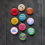 A bunch of colorful social justice pinback buttons on black denim, with messages such as: Abortion Is Healthcare, Disability Rights Are Human Rights, Housing Is A Human Right, There is Power In A Union, Support Trans Kids, Climate Action Now, Ceasefire and more.