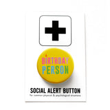 Round yellow pinback button that reads BIRTHDAY PERSON in alteranting pink & purple text, and blue and green text. with the I as a little candle. The button is pinned to a Social Alert Button backing card.