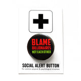 A round black 1.25" pinback button that reads PBLAME BILLIONAIRES, NOT EACH OTHER in red and green text. Badge is pinned to a Social Alert Button backing card.