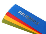 Four bright colored bookmarks fanned out, the top one is a bright blue bookmark that reads BIBLIOPHILE in silver embossed text.And there is an orange-red, marigold yellow and deep moss green bookmarks fanned below, with no visible text.