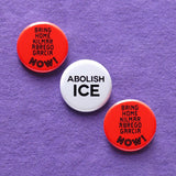 Three  1.25" pinback buttons in a diagonal line, first and last buttons are round red-orange 1.25" pinback buttons that reads BRING HOME KILMAR ABREGO GARCIA NOW! The middle button is white with black text that reads ABOLISH ICE. Buttons are pinned to a lavender cotton bag.