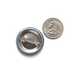 back of a metal pinback button next to a quarter for size