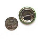 back of a round metal pinback next to a quarter for seize comparison
