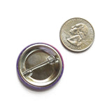 Back of a metal pinback button next to a quarter coin