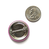 Back of a metal pinback button next to a quarter for size 