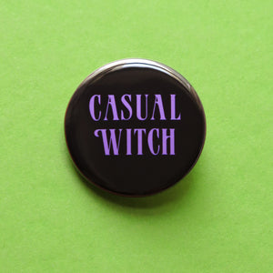 Round black pinback button that reads CASUAL WITCH in a lavender vintage 70’s font. Button is on a lime green background.