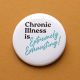 A round white pinback button that reads CHRONIC ILLNESS IS EXTREMELY EXHAUSTING in aqua & black text, that are retro 80's fonts. Button is on a Carmel colored backdrop.