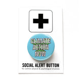 Round pinback button that says CLIMATE CHANGE NOW. White text on a light blue background, with pale green action lines. Button is on a Social Alert Button backing card.