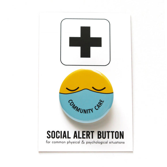 Round button with a yellow emoji face with closed eyes, wearing a mint green mask that reads COMMUNITY CARE in the shape of a smile. Button is on a Social Alert Button backing card.