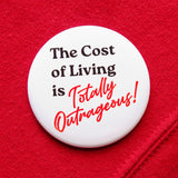 A round white  pinback button that reads THE COST OF LIVING IS TOTALLY OUTRAGEOUS in black & red text,  in two fonts, with a retro 80's vibe.  Button is on a red sweatshirt.