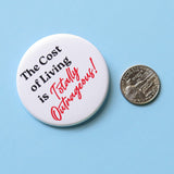 A round white  pinback button that reads THE COST OF LIVING IS TOTALLY OUTRAGEOUS in black & red text,  in two fonts, with a retro 80's vibe.  Button is on a baby blue background next to a quarter for size scale.