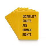 A fanned stack of golden yellow, vertical rectangle sticker with rounded corners that reads DISABILITY RIGHTS ARE HUMAN RIGHTS in a black san serif text.