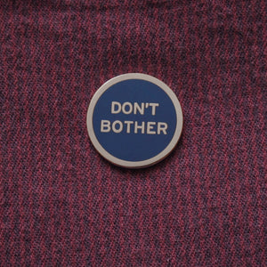 Round enamel pin that says DON'T BOTHER. Silver text and outline on a navy blue background