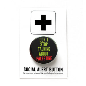A round black pinback button that reads DONT STOP TALKING ABOUT PALESTINE in green & red text. Button is held in a hand.
