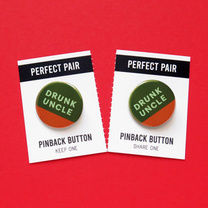 Two round pinback buttons, dark green background, mint green text that reads DRUNK UNCLE and a little half moon of whisky orange-brown at the bottom, to look like a partially drunk cup of whiskey. These buttons are on a perforated backing card that tears down the middle. Each Half reds PERFECT PAIR, Pinback Button, left side reads KEEP ONE. Right side reads SHARE ONE.