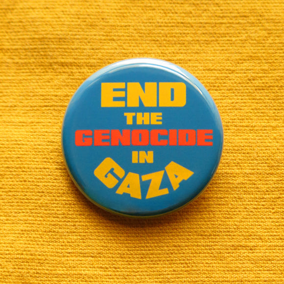 A round blue pinback button that reads END THE GEN0CIDE IN GAZA in yellow & orange bold text. Pinned to a goldenrod yellow cotton fabric.