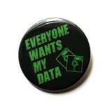 A round black  pinback button that reads EVERYONE WANTS MY DATA  in neon green text, in a 90's or Y2K vintage computer monitor vibe, with an illustrator of two little floppy discs in the lower right hand corner.  