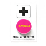 Round pink pinback button that reads FEMINIST in yellow san serif text. Badge is on a Social Alert Button backing card.