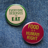 2 round pinback buttons, top one is cream with a green outline and green text that reads: Everyone Deserves To Eat, below is a burgundy 1.25"  pinback button that reads FOOD IS A HUMAN RIGHT in lime green text.  