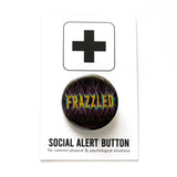 A round black button with tight thready yellow pink & blue  text that reads FRAZZLED. Button is on a Social Alert Backing Card.